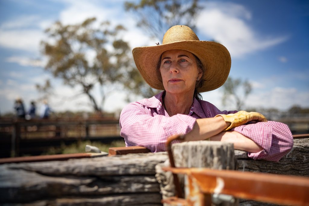 Woman in a pink shirt and broad-brimmed hat leaning on a timber fence