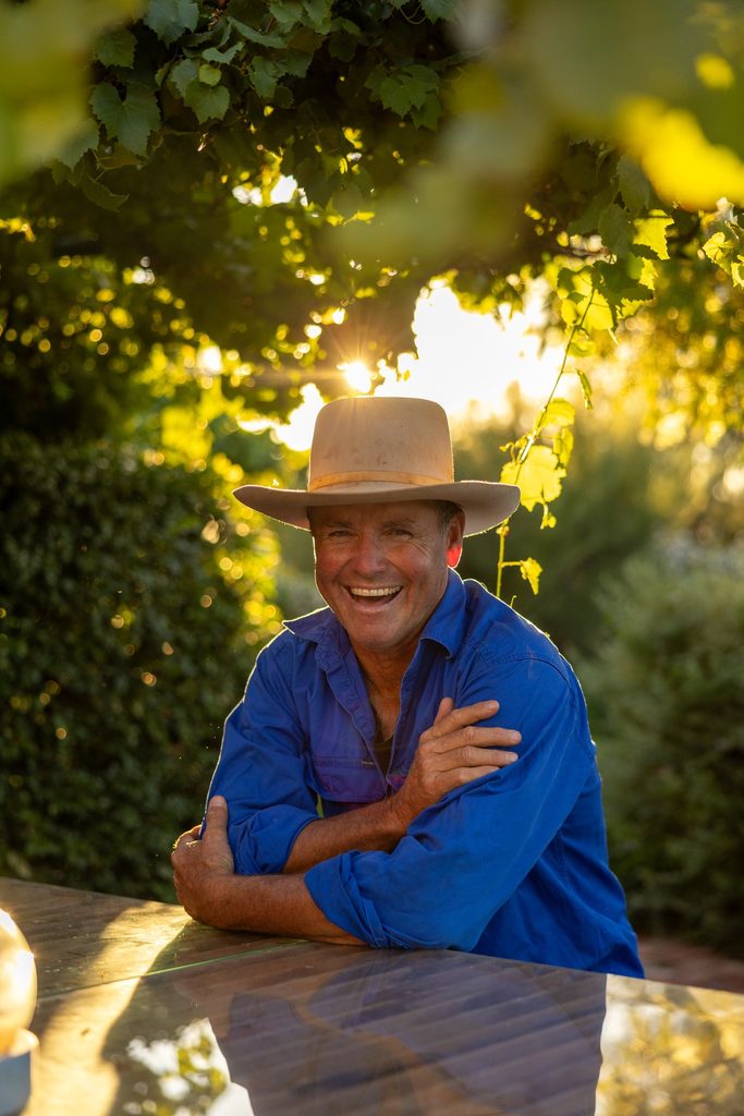 Man in a blue shirt and hat seated in a shaded garden