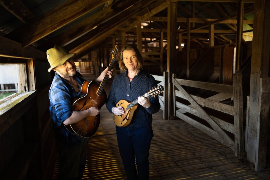 Two musicians playing string instruments in a timber shed