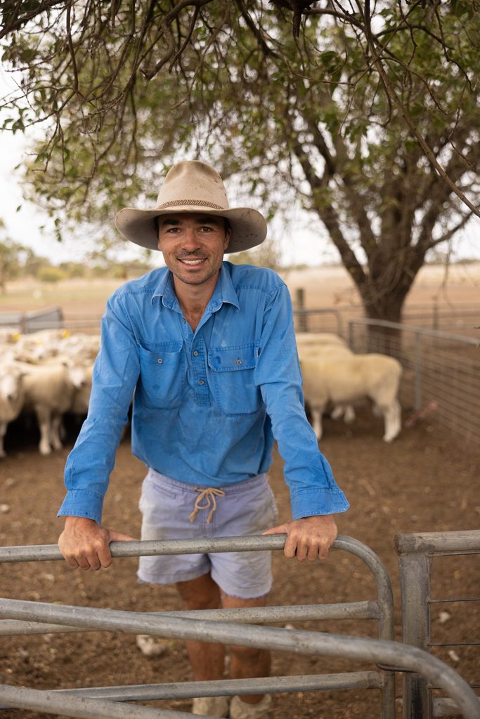 Man in a blue shirt leaning on a livestock yard rail